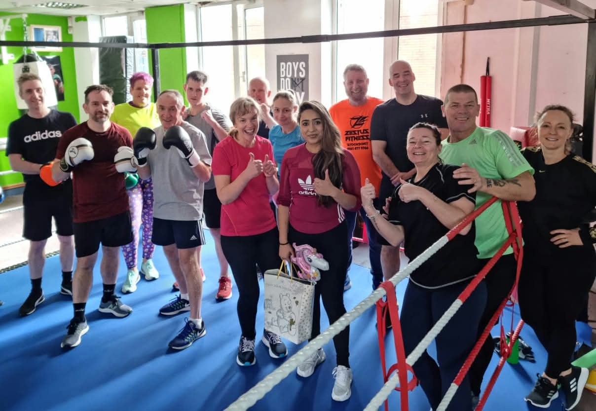 A friendly group of all ages giving thumbs up in the boxing ring.